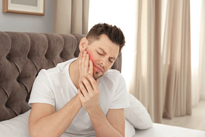 Man with jaw pain sitting up in bed